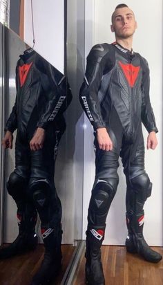 a man standing in front of a mirror wearing a black and red motorcycle suit