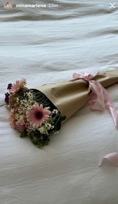 a bouquet of flowers wrapped in brown paper on top of a white sheeted bed