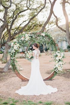 a woman in a wedding dress standing under an archway with white flowers and greenery