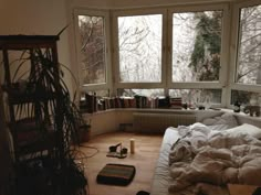 an unmade bed sitting in front of two windows next to a bookshelf