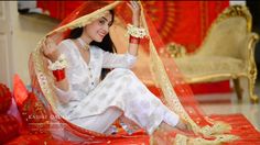 a woman sitting on top of a bed covered in red and gold cloths with her hands behind her head