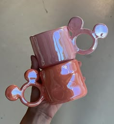 a hand holding a pink and brown mickey mouse coffee mug in it's palm