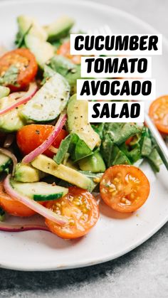 a white plate topped with cucumber, tomato and avocado salad next to a fork