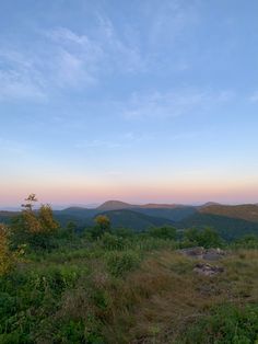 the sun is setting over the mountains and trees in the foreground, as seen from an overlook