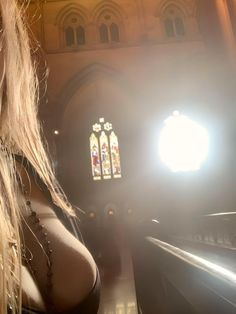 a woman standing in front of a church window with sunlight streaming through the window and her long blonde hair blowing in the wind