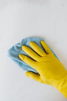 a person wearing yellow rubber gloves with a blue cloth on their palm and cleaning the surface