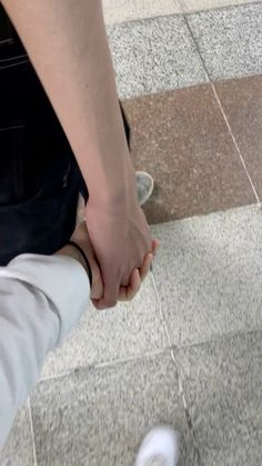 two people holding hands while standing next to each other on a tile floor in an airport