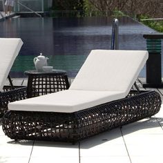 two chaise lounge chairs sitting next to each other on a tile floor near a body of water