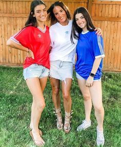 three girls are posing for the camera in front of a wooden fence and grass area