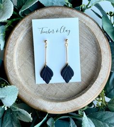 a pair of earrings with black leaves on them sitting on top of a wooden plate