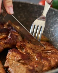 a person is cutting up some meat with a knife and fork in a skillet