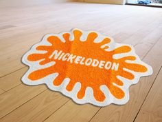 an orange and white rug with the word nickeleoden on it in front of a wooden floor