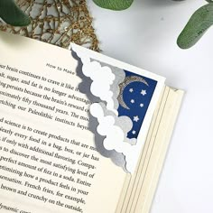 an open book sitting on top of a table next to a plant and some leaves