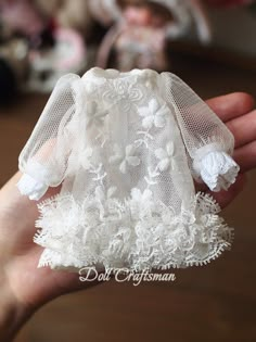 a hand holding a doll with white lace on it