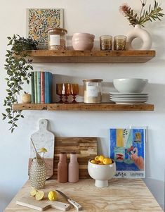 two wooden shelves filled with dishes and vases on top of a table next to books