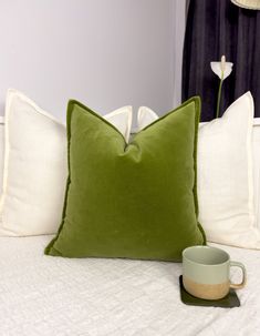 a green pillow sitting on top of a bed next to a cup and saucer