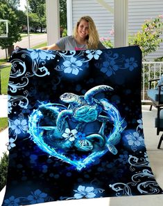 a woman holding up a blanket with a turtle in the middle of it and blue flowers on