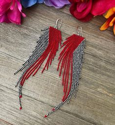 two pairs of red and black beaded tassels on wooden table next to flowers