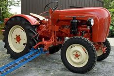 an old red farmall tractor parked in front of a building with a blue trailer attached to it