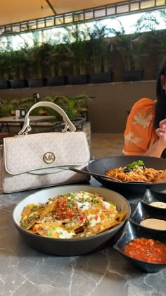 a woman sitting at a table filled with plates of food next to a handbag