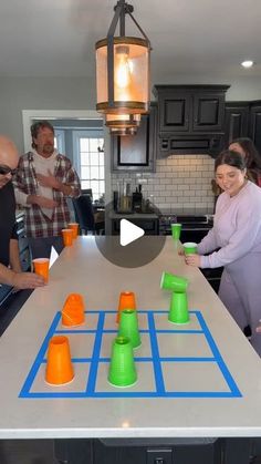 a group of people standing around a kitchen table with cups on it and an orange cup in the middle