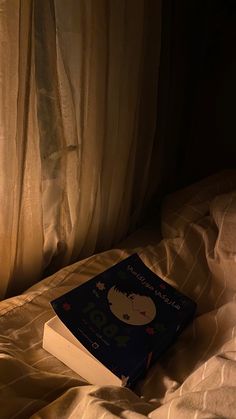 an open book sitting on top of a bed next to a window with sheer curtains