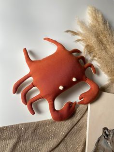 an orange crab shaped object sitting on top of a table next to a feathery plant