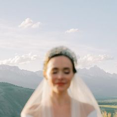 a woman in a wedding dress and veil looking at the camera with mountains in the background