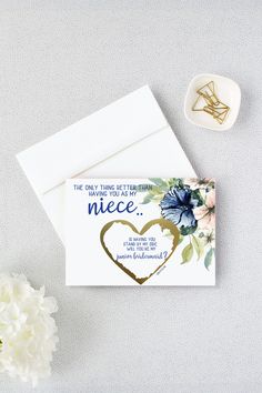 a card with a heart on it next to some flowers and a white flower pot