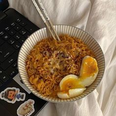 a bowl of noodles and eggs with chopsticks in front of a laptop computer