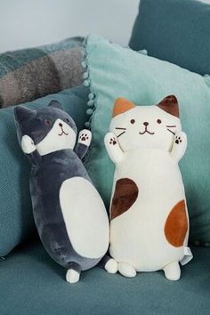 two stuffed cats sitting on top of a couch next to each other in front of pillows