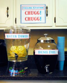 there is a pitcher and cups on the counter with signs above it that say chug chug, water tower, diesel fuel