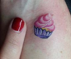 a small cupcake tattoo on the left side of her right hand, next to a red manicure