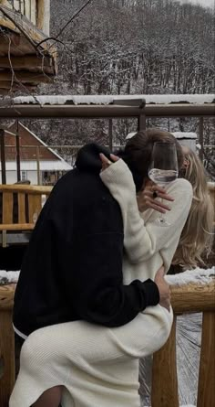 a man and woman kissing while holding a glass of wine in front of snow covered mountains