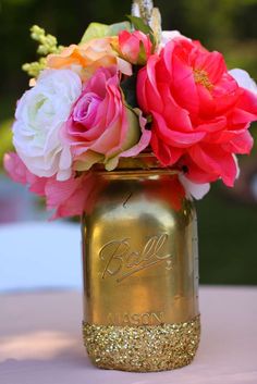 a gold mason jar with pink and white flowers in it sitting on top of a table