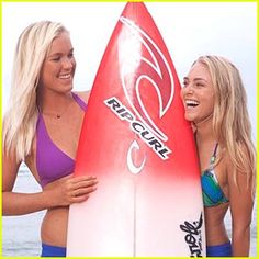 two beautiful women standing next to each other holding a surfboard