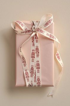 a pink wrapped gift with white ribbon and red robot designs on it, tied to a wall