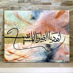 a painting with arabic writing on it in front of a brick wall and stone fireplace