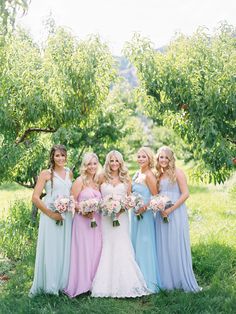 a group of women standing next to each other in front of trees and grass holding bouquets