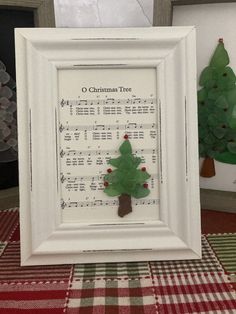 a christmas tree made out of sheet music is displayed in a white frame on a checkered tablecloth