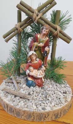 a nativity scene is displayed on a wooden table with rocks and pine branches in the foreground