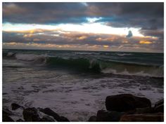 the ocean waves are crashing against the rocks and clouds in the sky over the water