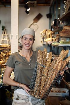 a woman holding a basket full of bread in a bakery shop with other items behind her