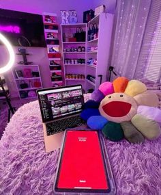 a laptop computer sitting on top of a bed next to a stuffed animal and cell phone