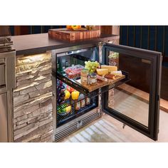 an open refrigerator filled with lots of food next to a stone wall and counter top