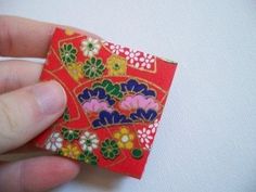 a hand holding a small piece of red paper with colorful flowers on it and a white background