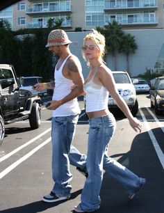 a man and woman walking across a parking lot next to each other with cars in the background