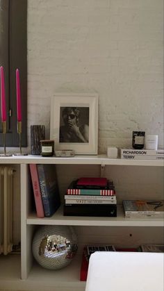 a shelf with books, candles and pictures on it