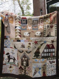 a quilt hanging on the side of a brick building in front of a window with trees