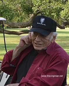 an old man sitting in a golf cart talking on his cell phone while wearing a hat